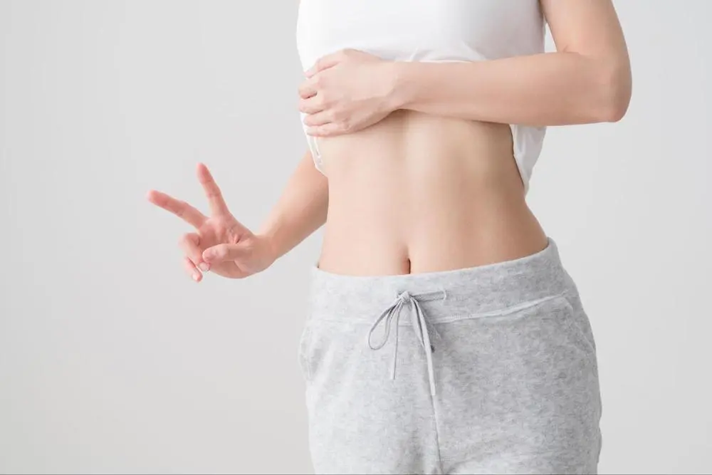 お腹を見せてピースサインをする女性